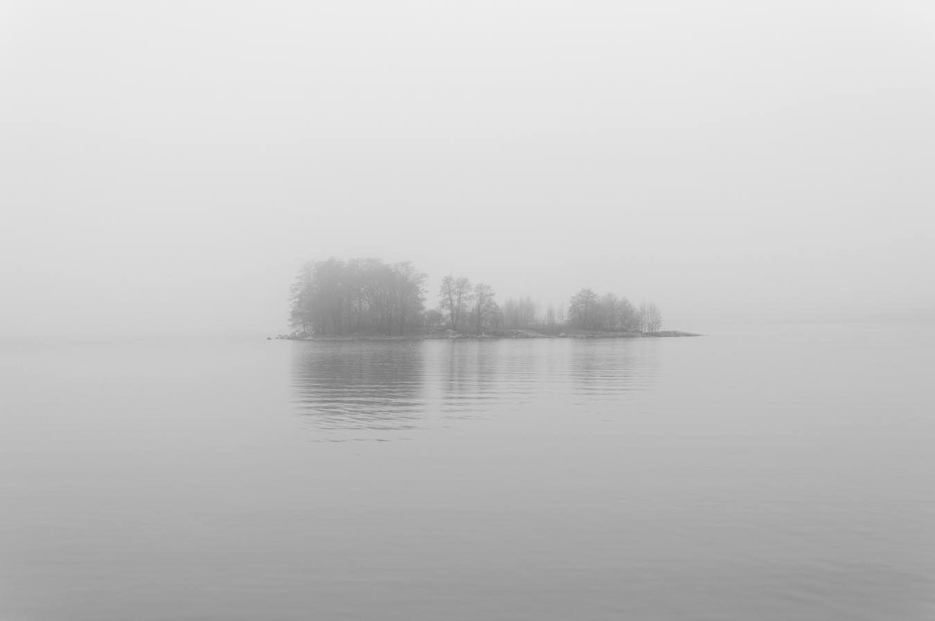 Una isla pequeña entre la niebla, sobre un lago en calma.